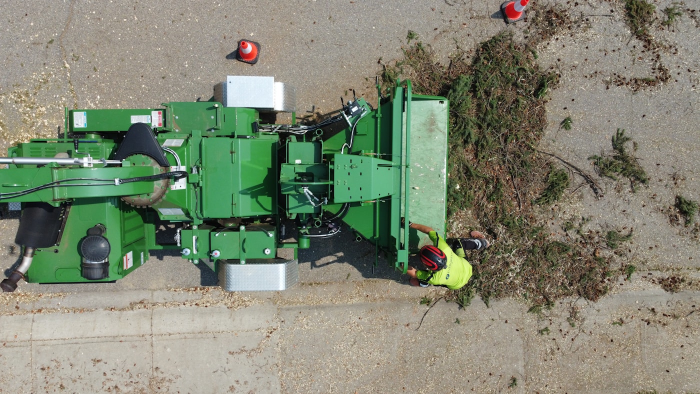 Crew processing a pile of yard branches with a wood chipper on a paved residential area