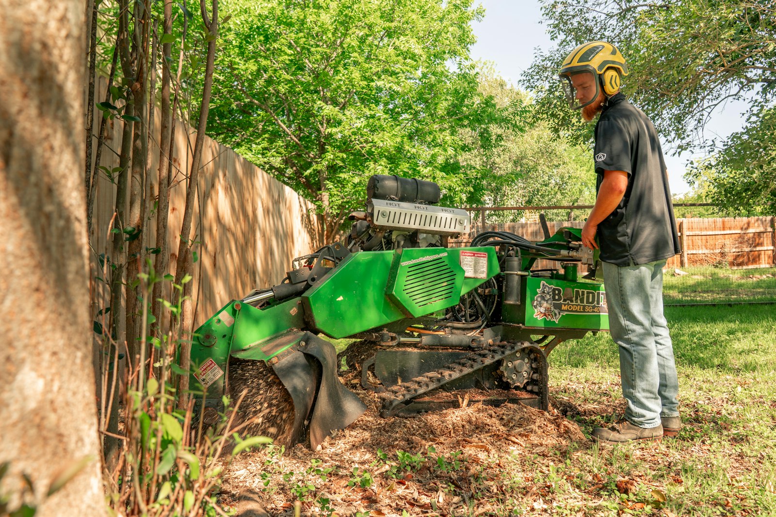 Operator grinding a residential tree stump beside a fence