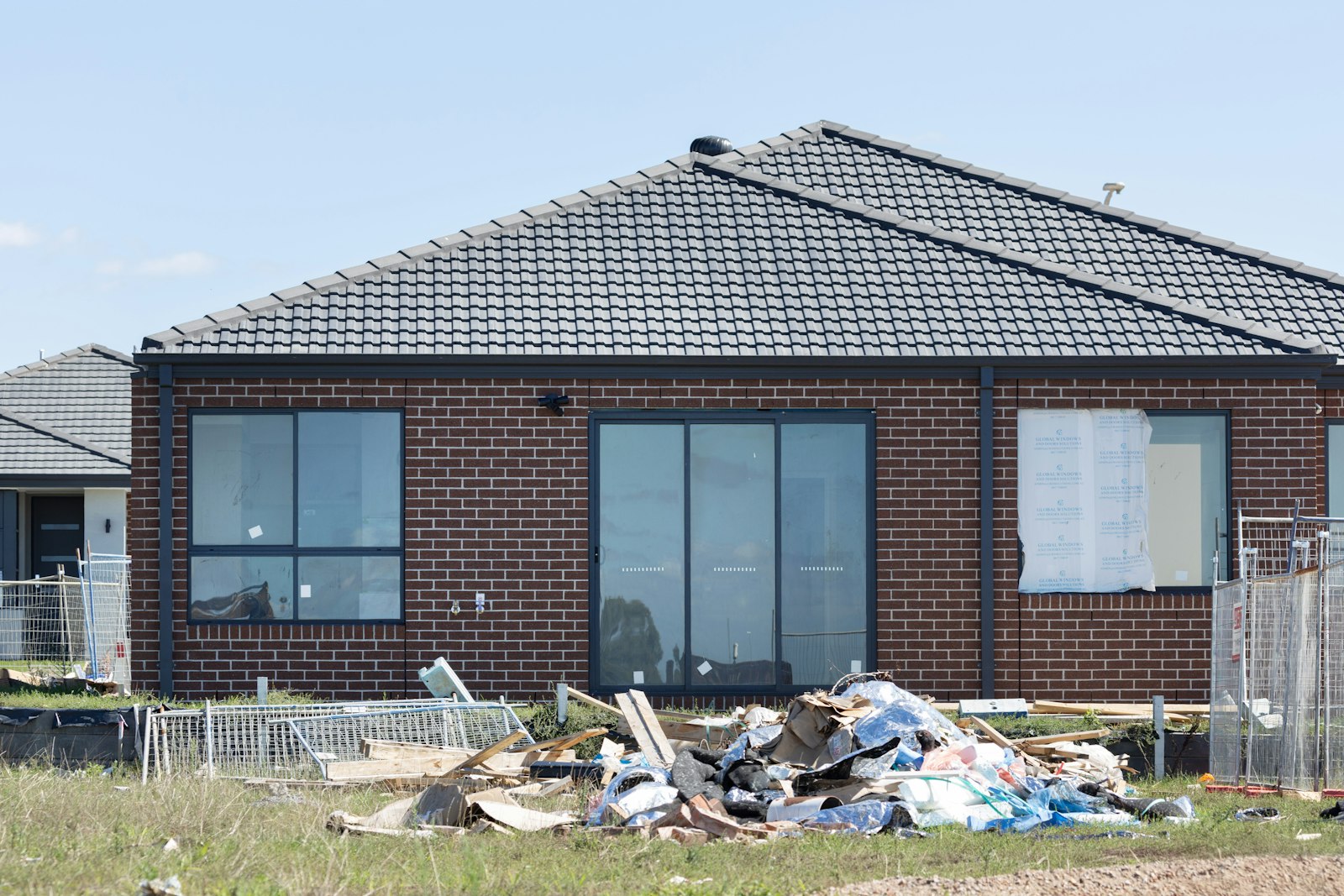 Pile of construction debris and cardboard in front of a brick house with an unfinished yard